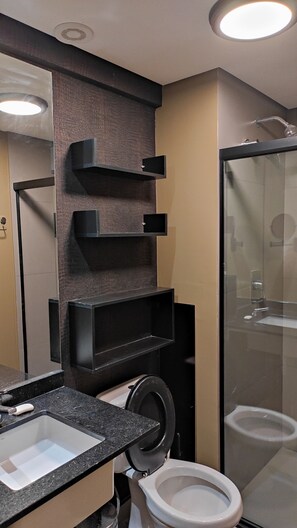 A modern bathroom with a black countertop, a white sink, a toilet, and a glass shower enclosure.