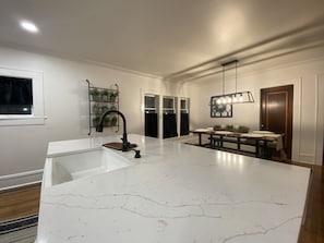 A modern kitchen with a large island, white marble countertops, a black faucet, and a hanging light fixture.