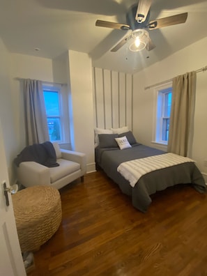 A bedroom with a bed, a chair, a window, and a ceiling fan.