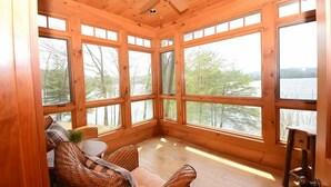 Una cabaña de madera con ventanas grandes, muebles de mimbre y un ventilador de techo.