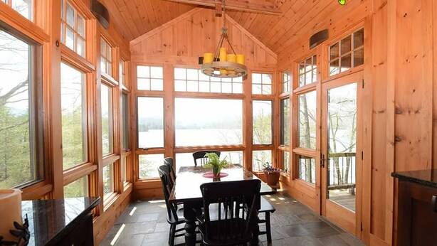 Una cabaña de madera con comedor, que incluye una mesa, sillas, ventanas amplias y vistas al exterior.