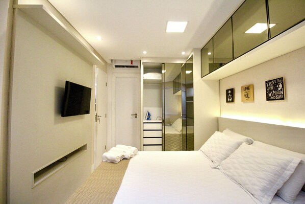 A hotel room with a bed, a TV mounted on the wall, a mirror, and a closet with sliding doors. - Fully furnished apartment with a pool, garage, and fitness center, located near Salvador's shopping district (Salvador)