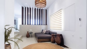 A modern bedroom with a bed, a woven rug, and a large window with blinds. - Wave an Idyllic Seafront Suite (Hersonissos)