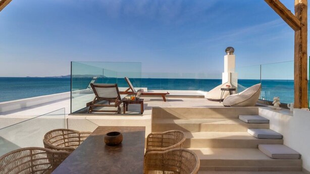 A terrace with wicker furniture, a table, and a fireplace overlooking the sea. - Wave an Idyllic Seafront Suite (Hersonissos)