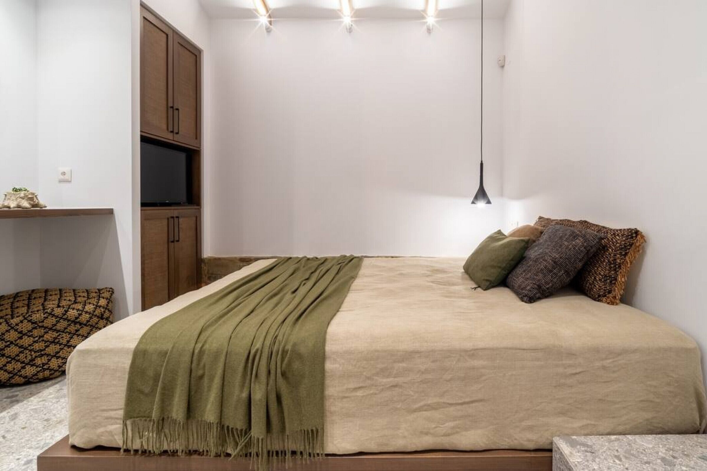 Une chambre à coucher comprenant un lit, une télévision, une armoire et un luminaire suspendu.