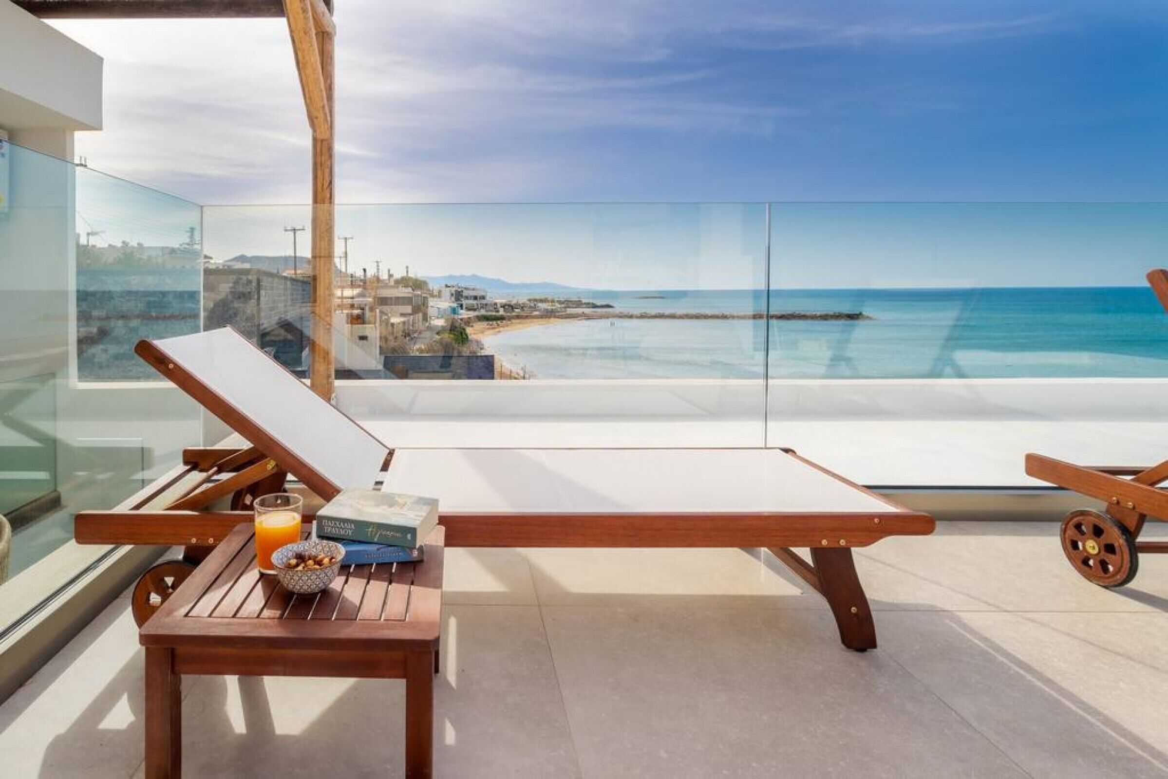 A balcony with a wooden table, a lounge chair, and a glass barrier.
