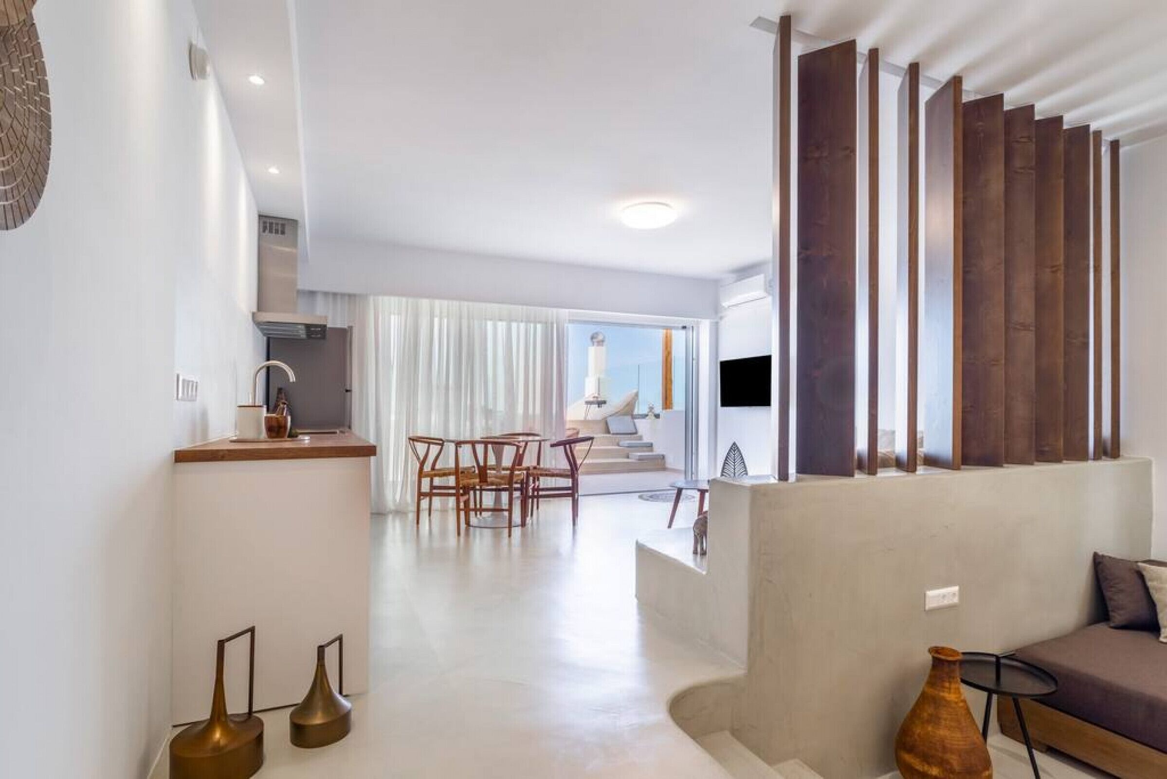 A modern living room with a sofa, a coffee table, and a dining area with chairs. There is a staircase leading to an upper floor.