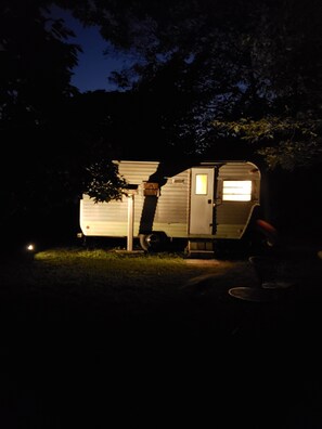 A small, single-story RV with a visible door and windows, parked in a grassy area at night. - Primitive Fannie Camper by River & Kettle Creek pa Renovo Pa Westport Pa. (Westport)
