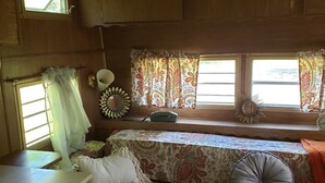 A cozy RV interior with a bed, a small desk, and a window with curtains.