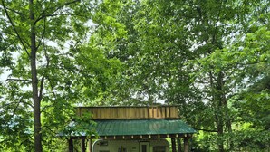 A green RV with a covered porch and a small table and chairs set up outside.