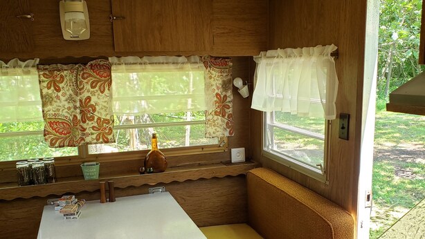 A compact RV kitchen with a central table, built-in seating, and a window with curtains.