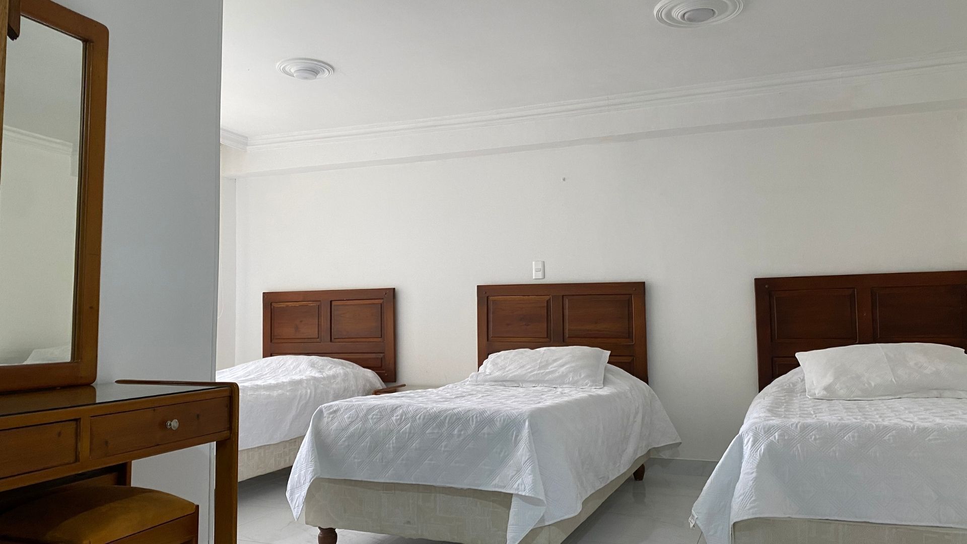 A hotel room with two single beds, a wooden dresser, and a large mirror.