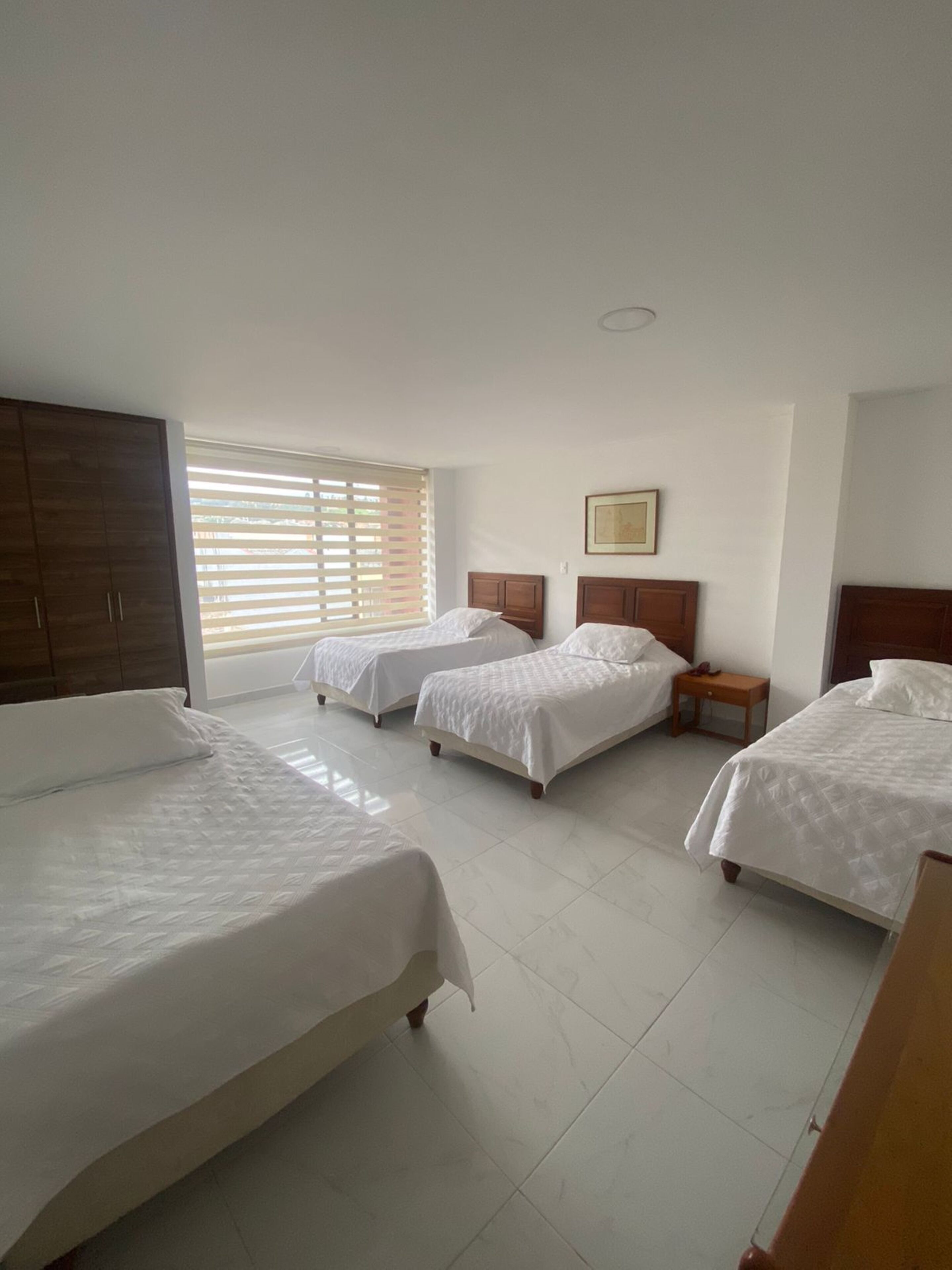 A bedroom with three single beds, a wardrobe, and a window with blinds.