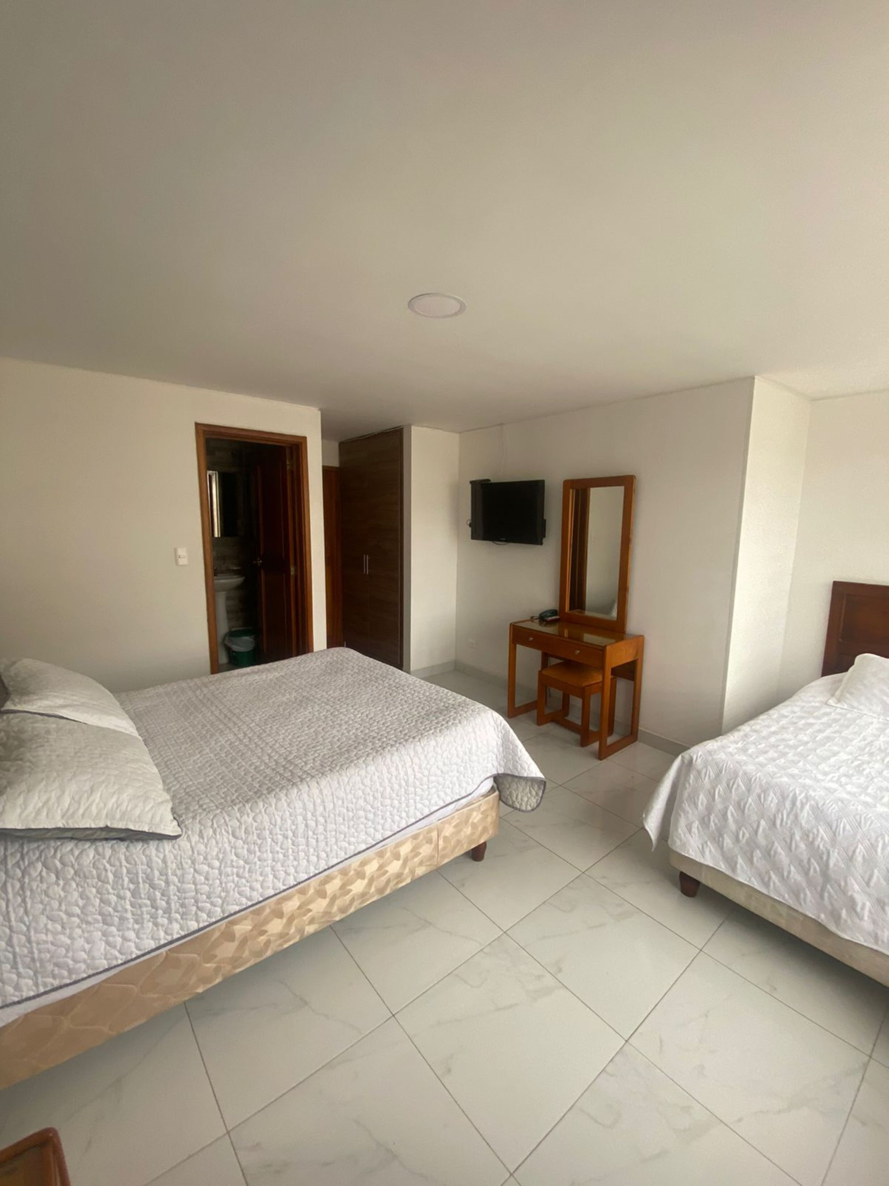 Habitación de hotel con dos camas, un escritorio de madera, televisor y armario.