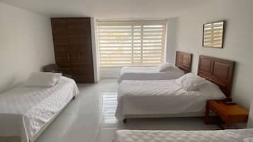 Une chambre d’hôtel avec deux lits simples, une armoire, une fenêtre avec des stores et une table de chevet avec une lampe.