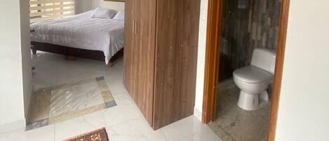 A bedroom with a bed, a wooden wardrobe, a bathroom with a toilet, and a shower.