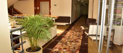 Un hall d’hôtel avec un tapis à motifs, une plante en pot, un escalier et un comptoir d’accueil.