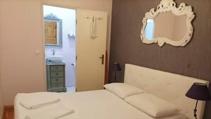 Een slaapkamer met een bed, nachtkastje, lamp, spiegel en een deur naar een badkamer.