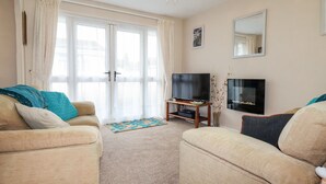 Ein Wohnzimmer mit einer Sofagarnitur, einem Fernseher, einem Spiegel und einem großen Fenster mit Vorhängen.
