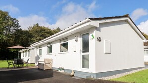 Ein eingeschossiges, weißes Gebäude mit flachem Dach, einer kleinen Veranda mit einer Bank und einem Tisch mit Stühlen.