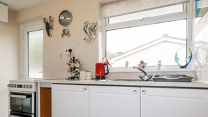 Eine Küche mit weißen Schränken, einem Herd, einer Spüle, Dekoration und einem Fenster mit Ausblick.