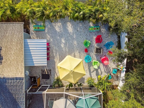 An outdoor patio area with a sandy surface, surrounded by greenery and various colorful umbrellas.