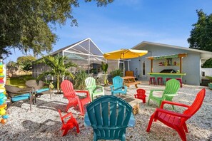 Un espace extérieur aménagé avec des chaises Adirondack aux couleurs vives, un patio couvert et un coin bar avec des tabourets.