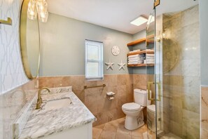 A bathroom with a marble sink, a toilet, a glass shower enclosure, and a towel rack with folded towels.