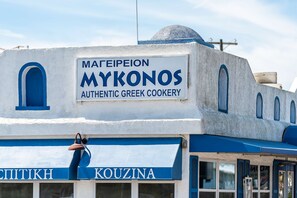 Un bâtiment sur lequel on peut lire l’inscription « MAΓEIEΠEION MYKONOS AUTHENTIC GREEK COOKERY » et, en dessous, le mot « KOUZINA ».
