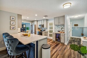 A modern kitchen with a central island, stainless steel appliances, and a dining area with bar stools. - Tropical Pool Retreat in Tarpon Springs (Tarpon Springs)