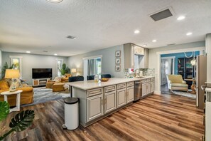 Una cocina moderna con una isla central, suelo de madera y un área de comedor con sofá y mesa.