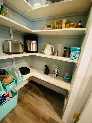Une cuisine équipée d’un grille-pain, d’une machine à café, d’une bouilloire et de différents récipients rangés sur des étagères.