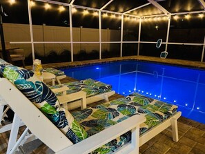A swimming pool with lounge chairs and string lights. - Tropical Pool Retreat in Tarpon Springs (Tarpon Springs)