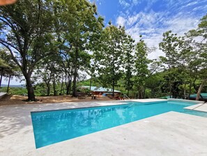 A swimming pool surrounded by trees, with a view of a building in the background. - Brand new Bungalow Mountain with Ocean Views (Pinilla)