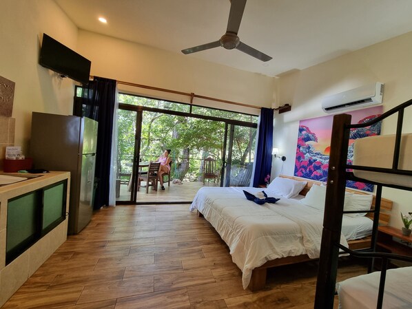 A hotel room with a bed, a desk, a TV, and a sliding glass door leading to an outdoor area with a table and chairs. - Brand new Bungalow Mountain with Ocean Views (Pinilla)