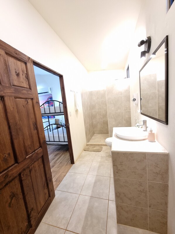 A bathroom with a wooden door, a shower area, and a sink with a mirror. - Brand new Bungalow Mountain with Ocean Views (Pinilla)