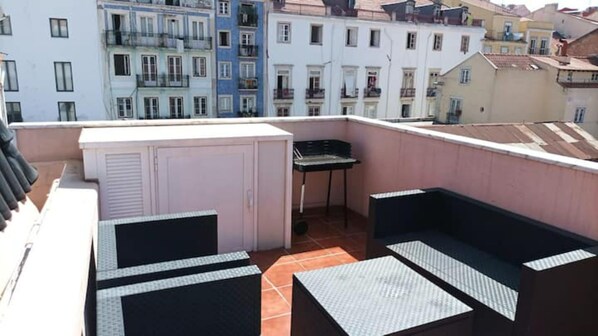 A rooftop terrace with a small table and chairs, a cabinet, and a view of neighboring buildings.