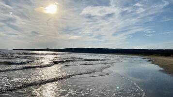 Ein Strand mit sanft rauschenden Wellen, einem klaren Himmel und einer fernen Küstenlinie.