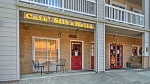 A two-story building with a cafe named 'Cafe' SilvaBella. There are two red doors, a balcony, and a small table with chairs outside. - Pine Mountain Club Getaway w/ Foosball Table! (Pine Mountain Club)