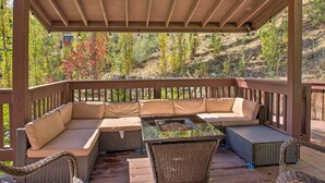 A covered outdoor seating area with a cushioned bench and wicker chairs, overlooking a wooded hillside. - Pine Mountain Club Getaway w/ Foosball Table! (Pine Mountain Club)