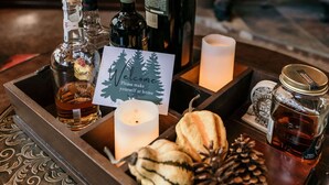 Una zona de bar con barra de madera, diferentes botellas, una vela y una tarjeta de bienvenida.