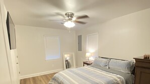 A bedroom with a bed, wooden flooring, a ceiling fan, and a nightstand with a lamp.