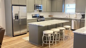 A modern kitchen with grey cabinets, stainless steel appliances, a central island with stools, and wooden flooring.