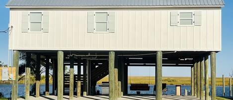 A two-story house with a metal roof, wooden pillars, and a dock extending into a body of water.