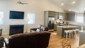A spacious living area with a brown leather sofa, a television, and a ceiling fan.