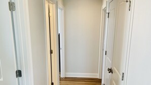 A hallway with white doors, wooden flooring, and a plain ceiling.