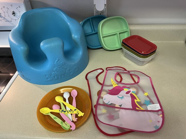 A kitchen counter with a blue silicone mold, a green and blue container, a stack of clear plastic containers, a bowl with colorful utensils, and a pink bag with a unicorn design. - Budget-friendly, family-oriented home. Minutes from Main Attractions! (Sevierville)