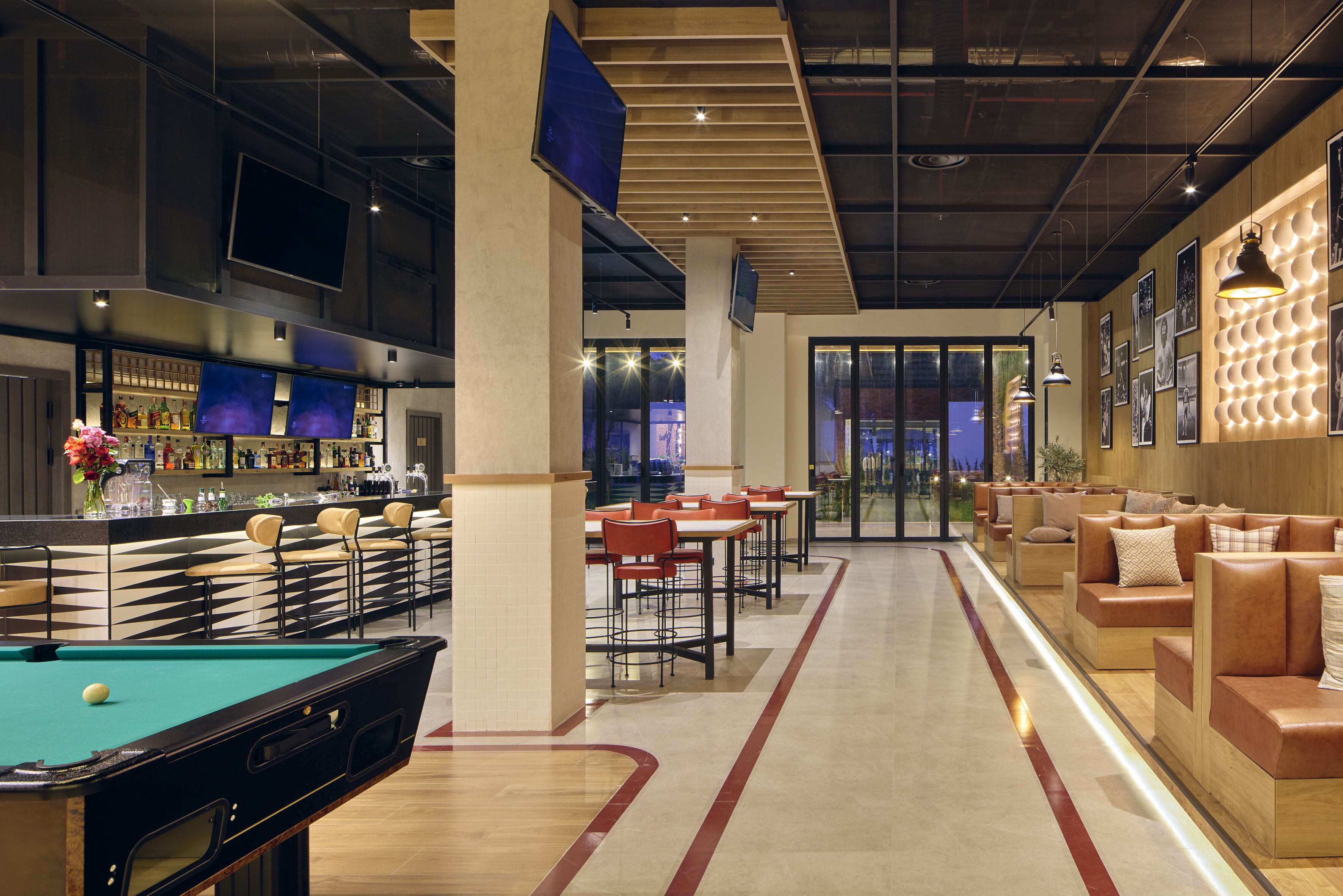 A modern bar area with a pool table, seating, and a bar counter with various bottles.