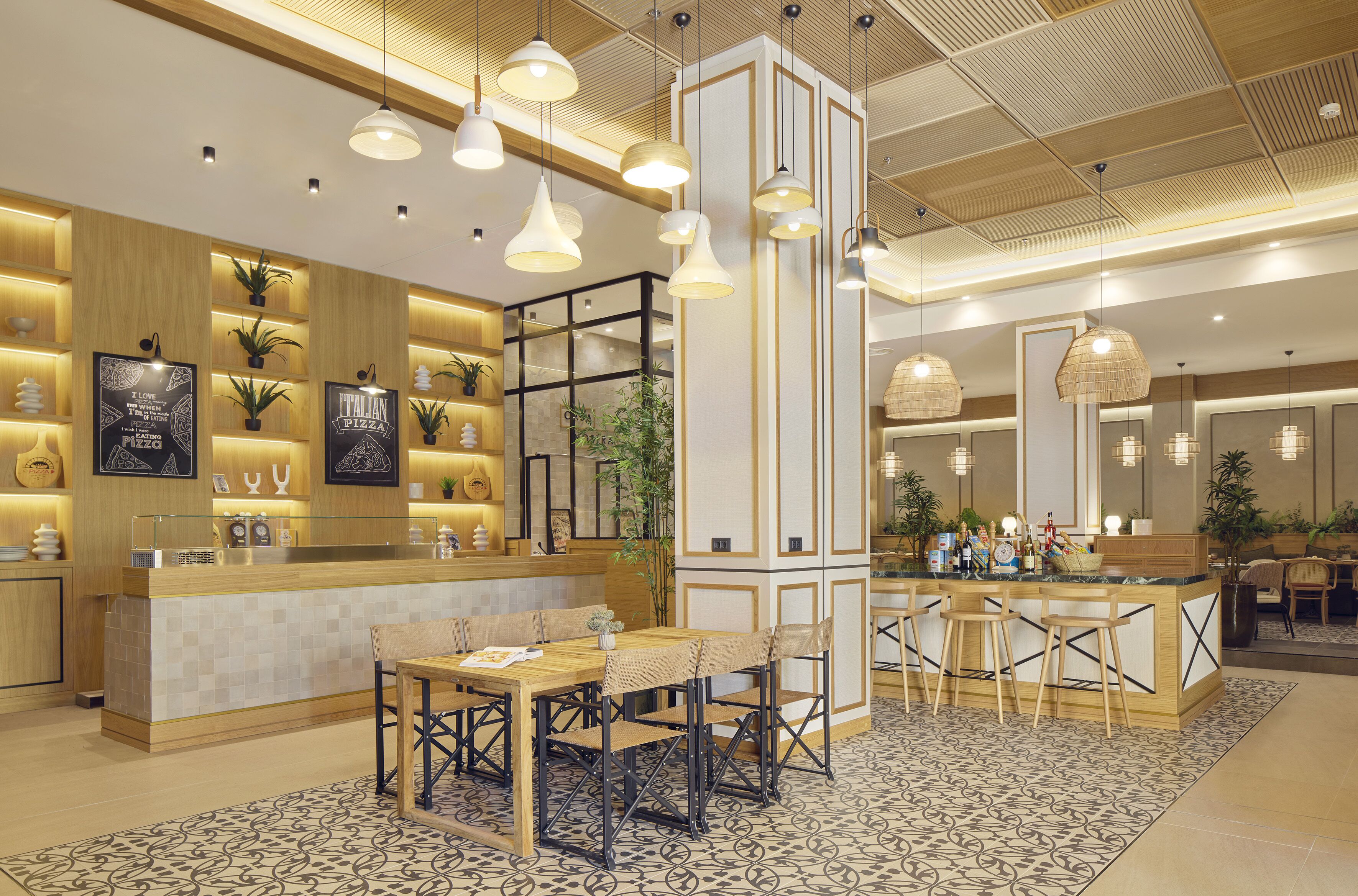 Um hall de hotel moderno com área de bar central, espaços para sentar e plantas decorativas.
