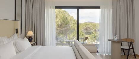 Habitación de hotel moderna con una cama grande, un balcón con mesa y sillas, y vistas al exterior.